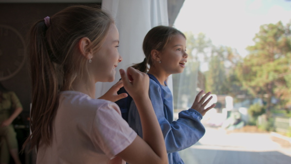 Two little sisters looking through the window indoors in a hotel.