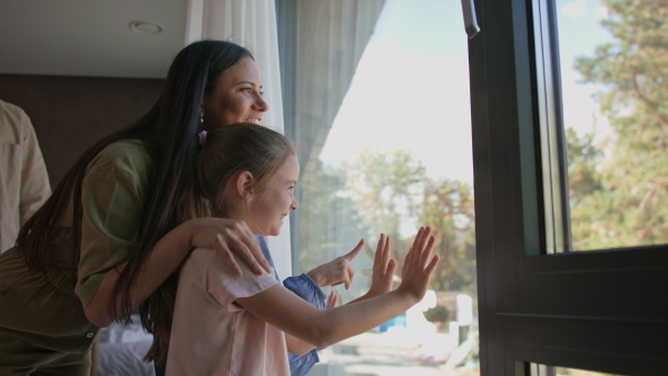 Two little sisters with mother looking through the window indoors in a hotel.