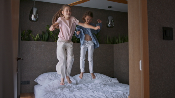 Two little sister jumping on a bed indoors in hotel.