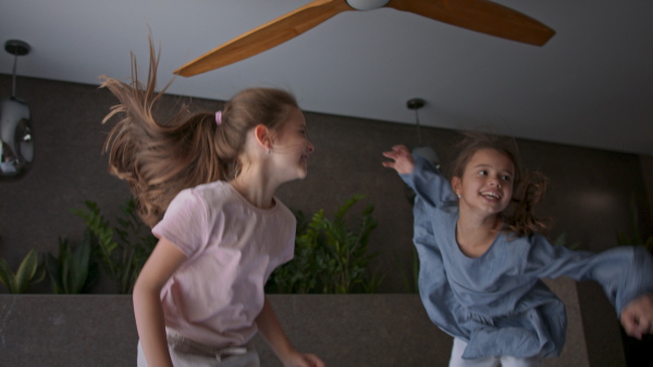 Two little sister jumping on a bed indoors in hotel.