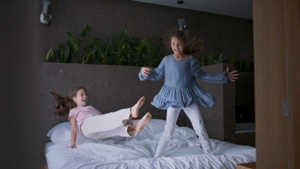 Two little sister jumping on a bed indoors in hotel.