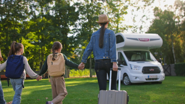 A rear view of young family with suitcases going to caravan outdoors at park.