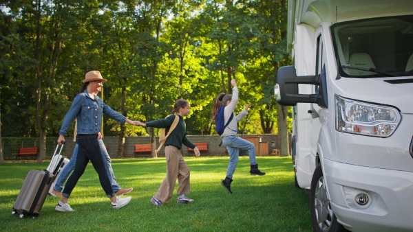 A side view of young family with suitcases going to caravan outdoors at park.