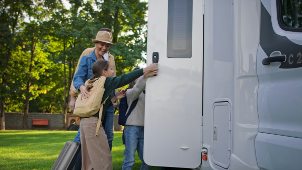 A side view of young family with suitcases going to caravan outdoors at park.