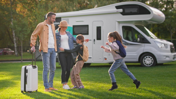 A rear view of young family with suitcases going to caravan outdoors at park.