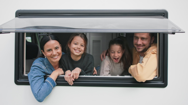 A happy young family with two children looking out of caravan window.