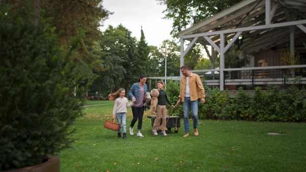 A happy young family with basket and blanket going to have picnic outdoors in restaurant area.