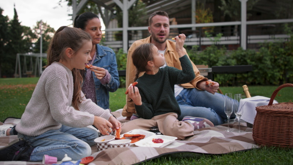 A happy young family sitting on blanket and having take away picnic outdoors in restaurant area.