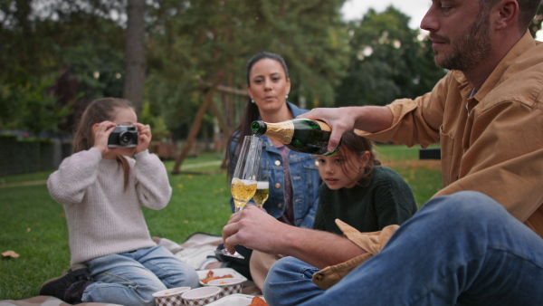 A happy young family sitting on blanket and having take away picnic outdoors in restaurant area.