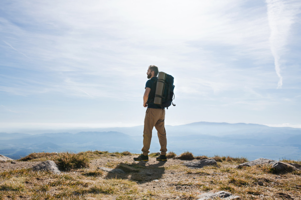 Rear view of mature man with backpack hiking in mountains in summer, resting.