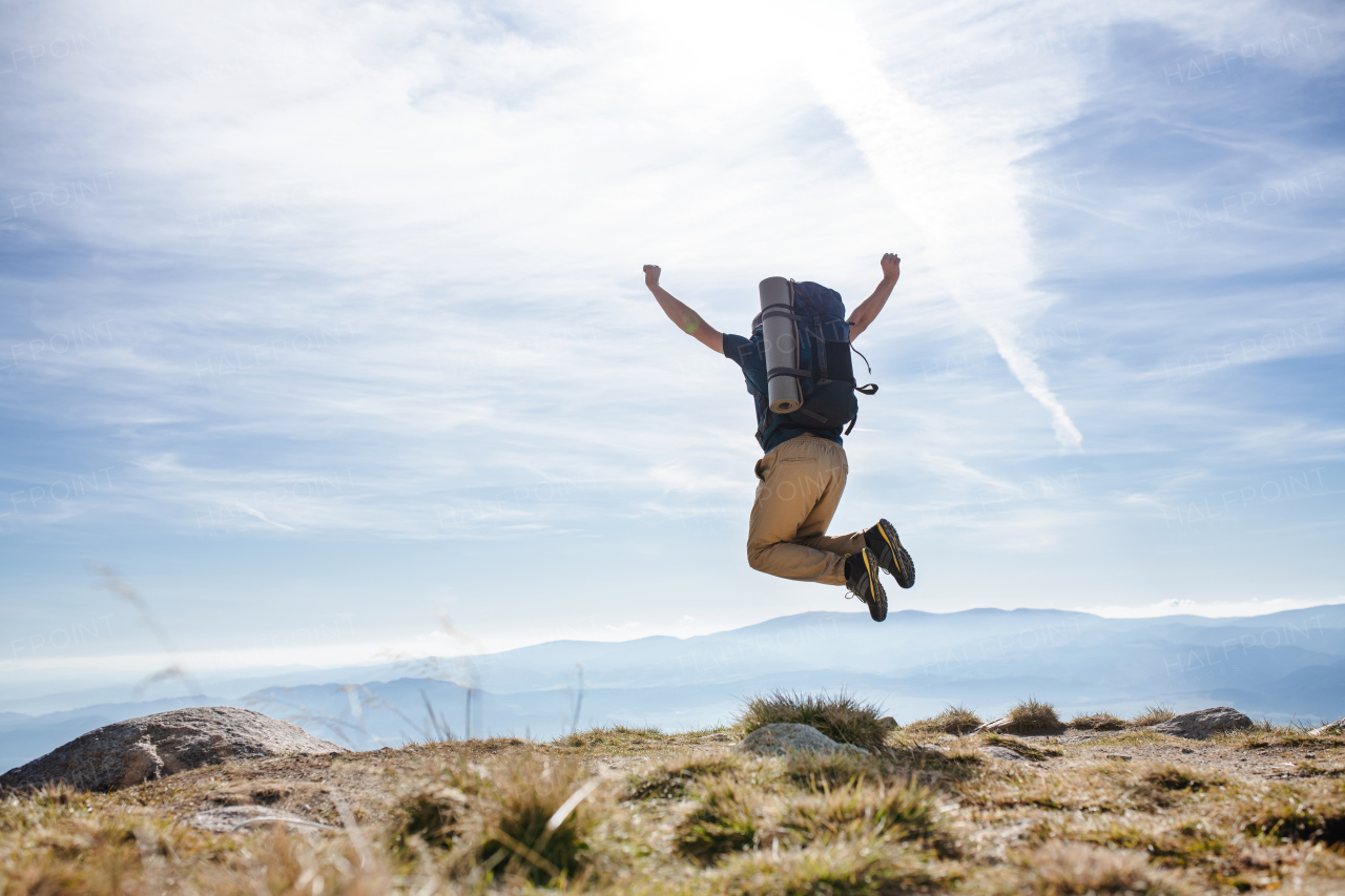 Rear view of mature man with backpack hiking in mountains in summer, jumping.