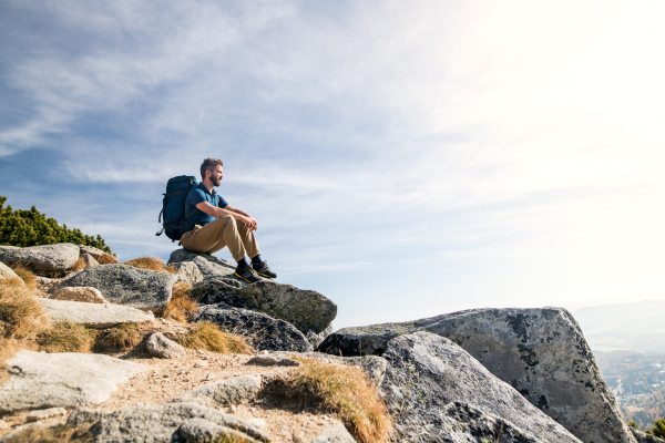 Mature man with backpack hiking in mountains in autumn, resting on rock.