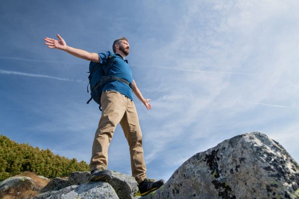 Mature man with backpack hiking in mountains in summer, resting and meditating with arms stretched.