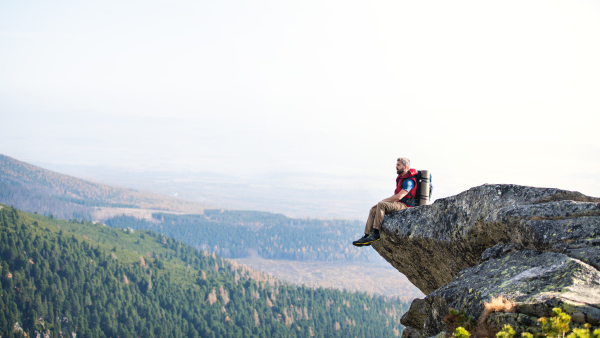 Mature man with backpack hiking in mountains in autumn, resting on rock. Copy space.