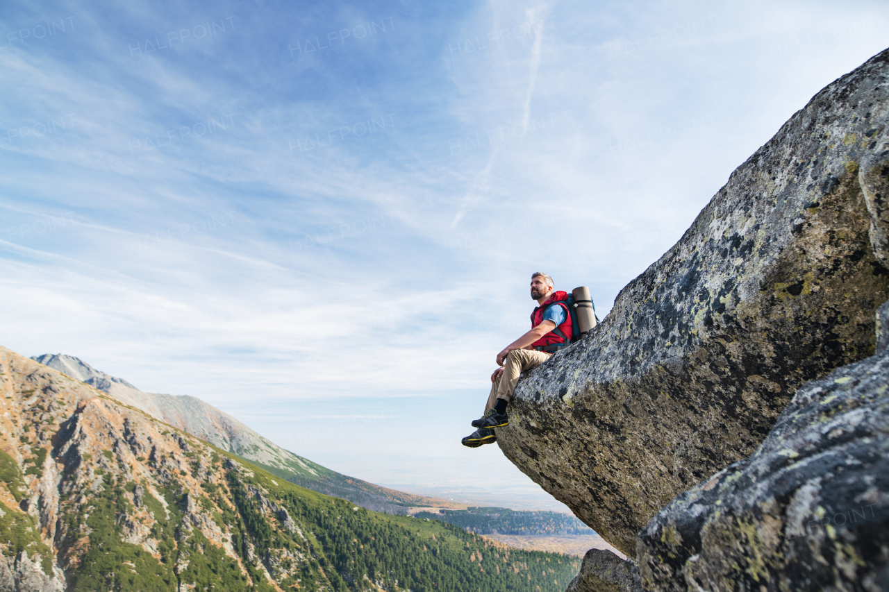 Mature man with backpack hiking in mountains in autumn, resting on rock.