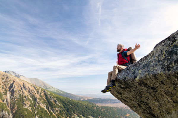 Mature man with backpack hiking in mountains in autumn, resting on rock. Copy space.