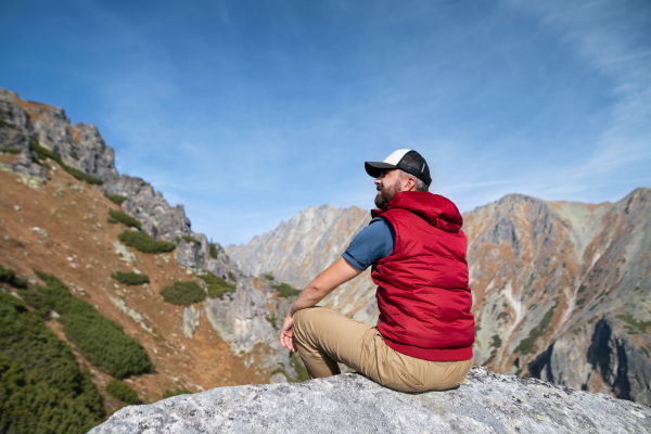 Rear view of mature man hiking in mountains in autumn, resting. Copy space.