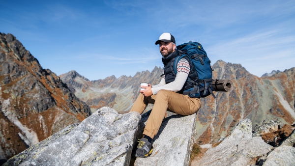 Mature man with backpack hiking in mountains in autumn, resting on rock.