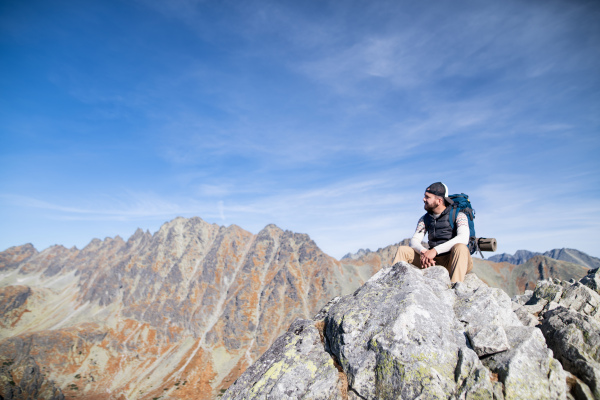 Mature man with backpack hiking in mountains in autumn, resting on rock. Copy space.