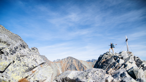 Mature man with backpack hiking in mountains in autumn, resting with arms stretched.