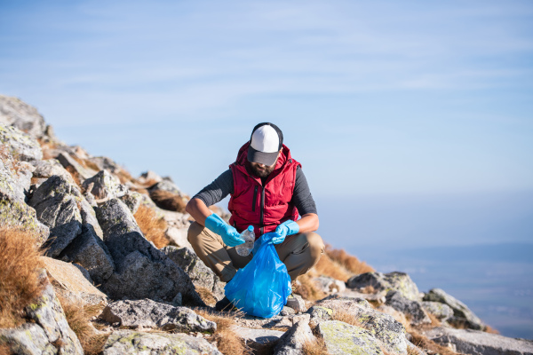 Mature man hiker picking up litter in nature in mountains, plogging concept.