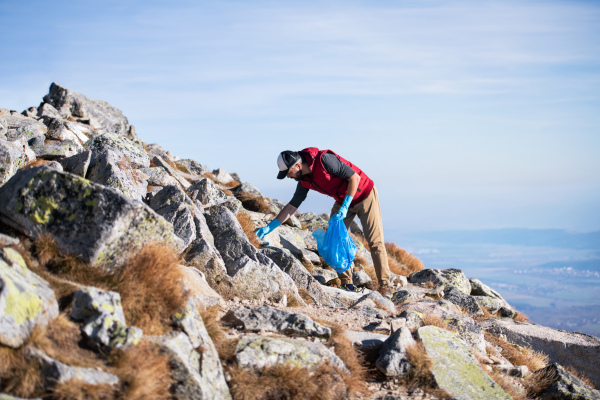 Mature man hiker picking up litter in nature in mountains, plogging concept.