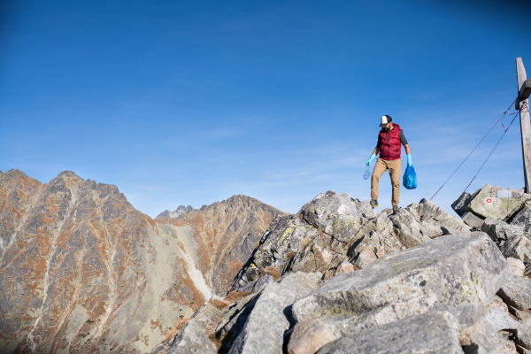 Mature man hiker picking up litter in nature in mountains, plogging concept.