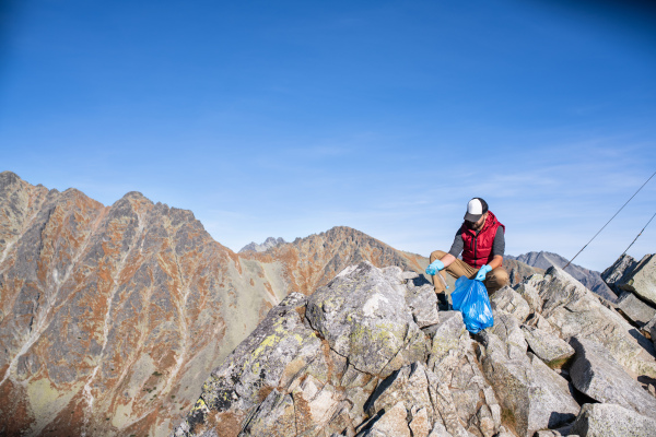 Mature man hiker picking up litter in nature in mountains, plogging concept.