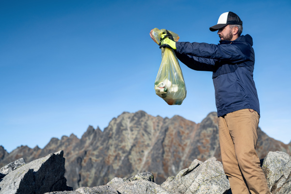 Mature man hiker picking up litter in nature in mountains, plogging concept.