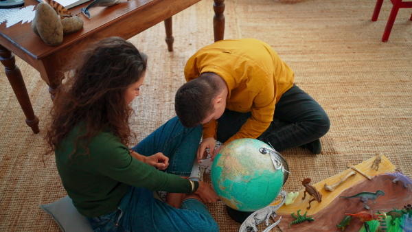 A young man with Down syndrome with his tutor using globe and learning about dinosaurs, homeschooling.