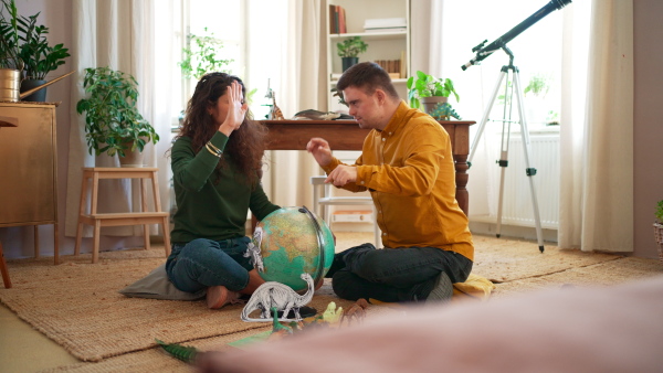 A young man with Down syndrome with his tutor using globe and learning about dinosaurs, homeschooling.