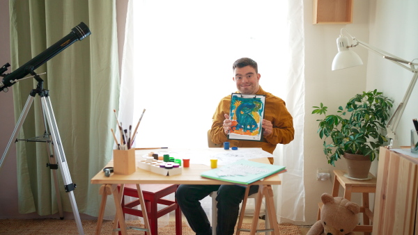 A young man with Down syndrome showing painting of dinosaur, homeschooling.