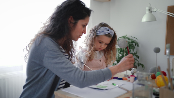 A little concentrated girl with her mother painting and making a solar system model at home, homeschooling.