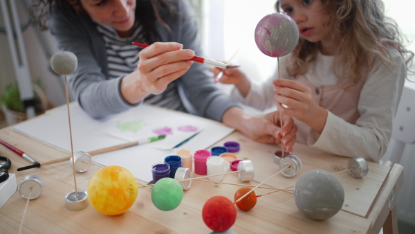 A little concentrated girl with her mother painting and making a solar system model at home, homeschooling.