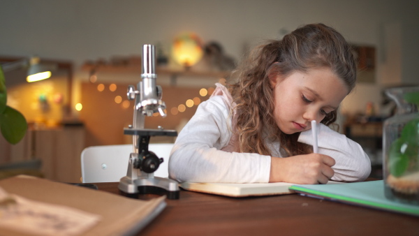 A concentrated little girl writing and making a herbarium, biology project indoors at home, homeschooling.