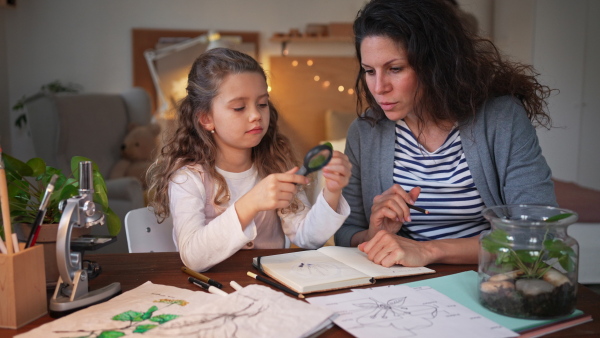 A concentrated little girl making a herbarium, biology project with her mother indoors at home, homeschooling.