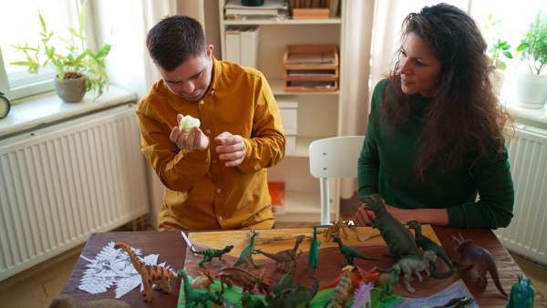 A young man with Down syndrome with his tutor learning about dinosaurs, homeschooling.