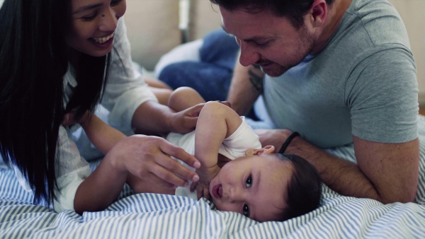 A young affectionate couple cuddling with a little baby indoors on bed.