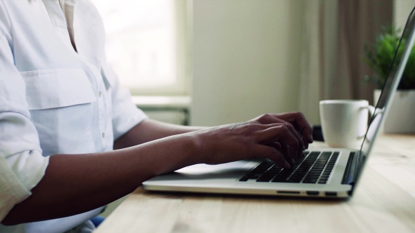 A midsection of young asian woman with laptop sitting at the desk indoors at home, typing.