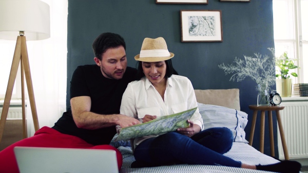 Young happy couple with map and laptop indoors at home, planning a trip or journey.