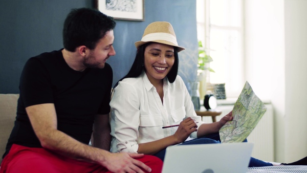 Young happy couple with map and laptop indoors at home, planning a trip or journey.