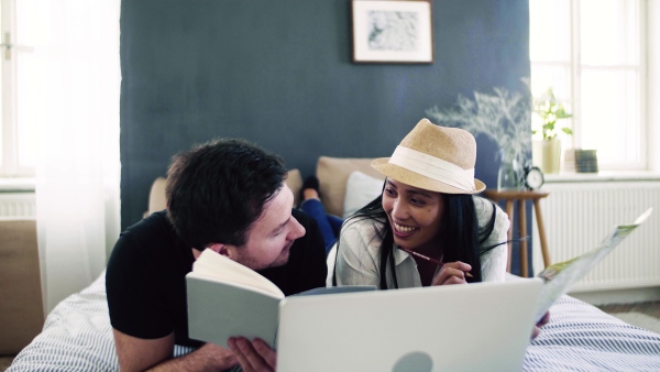 Young happy couple with map and laptop indoors at home, planning a journey.