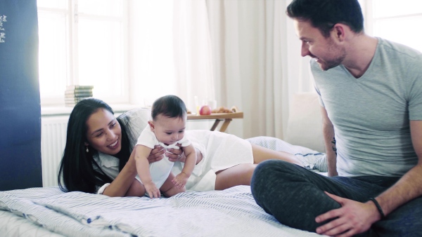 A young affectionate couple cuddling with a little baby indoors on bed.