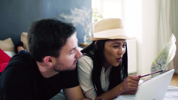 Young happy couple with map and laptop indoors at home, planning a journey.