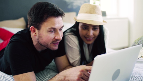 Young happy couple with map and laptop indoors at home, planning a journey.