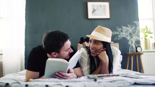 A young affectionate couple with book on bed indoors at home, talking.