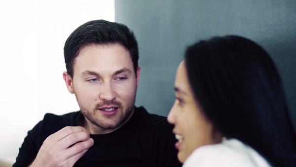 A close-up of young affectionate couple with coffee sitting indoors at home, talking.