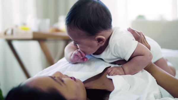 A young affectionate mother cuddling with a little baby indoors on bed.