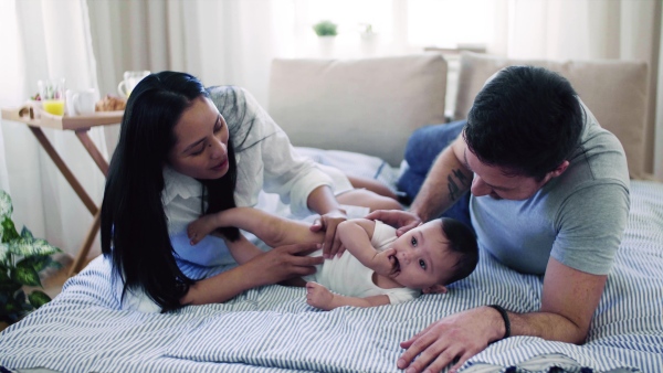 A young affectionate couple cuddling with a little baby indoors on bed.