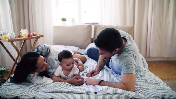 A young affectionate couple cuddling with a little baby indoors on bed. Slow motion.